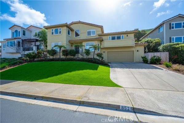 Two-story beige house with a garage, broad driveway, and bright green front lawn.