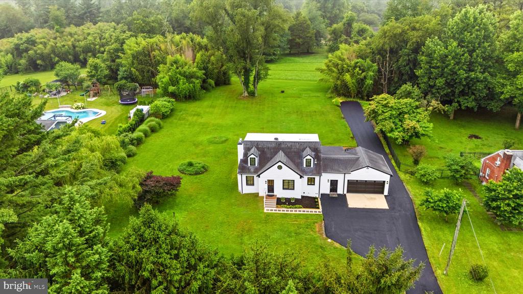 Aerial view of a white house on a large lawn, with a swimming pool and wooded surroundings.