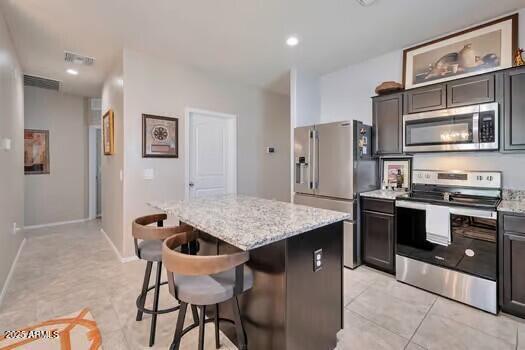 Kitchen with a speckled stone island, two bar stools, and stainless steel appliances.