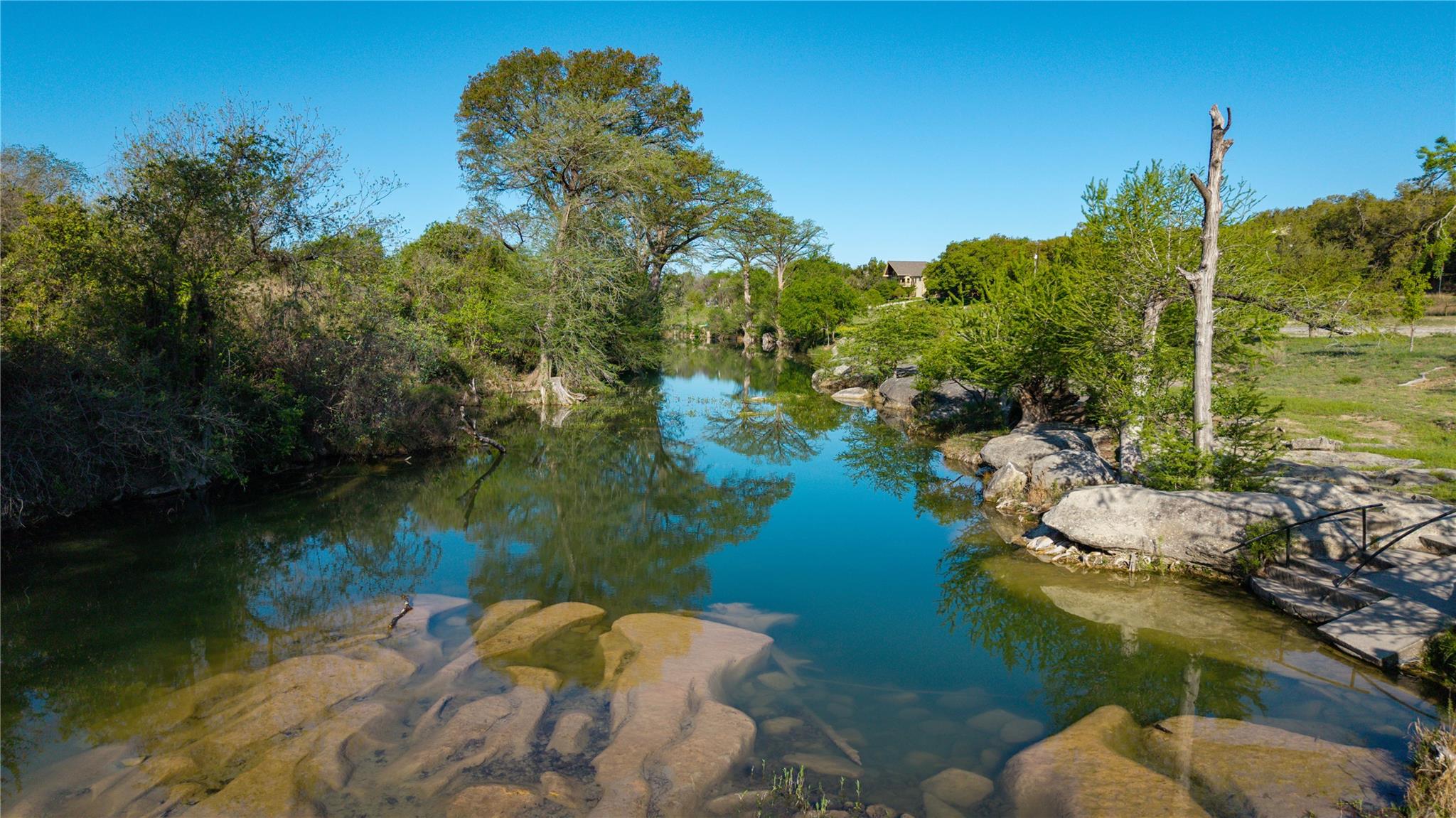 Clear creek bordered by trees and smooth limestone rocks, with a railed path along the bank.