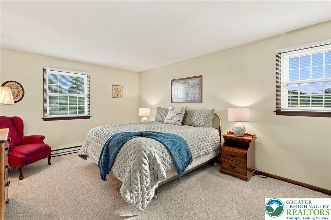 Bedroom with a quilted bed and blue throw, red armchair, and two windows.
