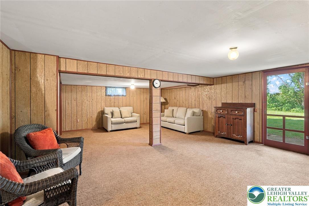Living room with wood-paneled walls, beige carpet, two seating areas, and a glass door to the yard.