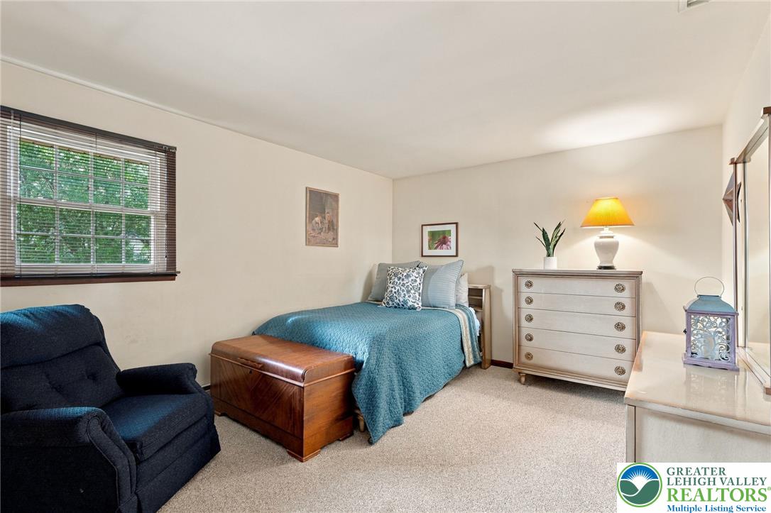 Furnished bedroom with a teal-covered bed, dark blue armchair, and cream dresser.