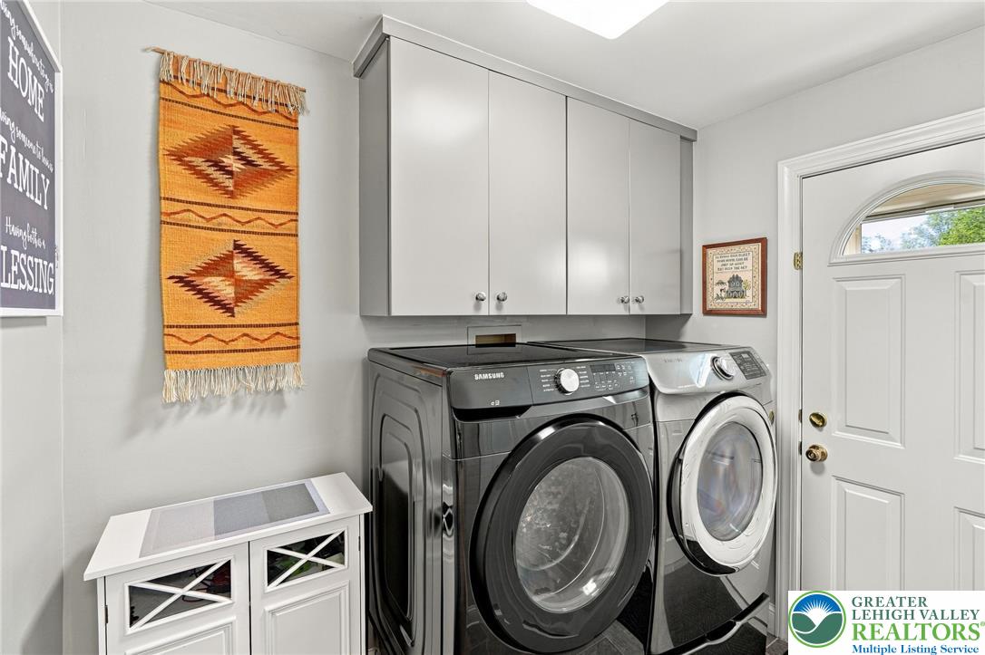 Laundry room with front-load washer and dryer beneath white cabinets, beside a white exterior door.