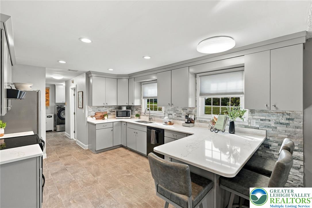 Updated kitchen with gray cabinetry, stone backsplash, and a large white peninsula with seating.