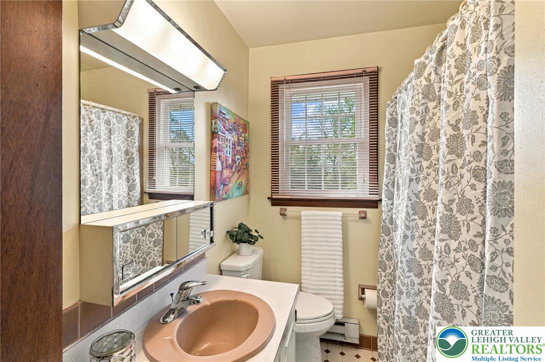Bathroom with peach sink, mirrored vanity, toilet, and floral-patterned shower curtain.