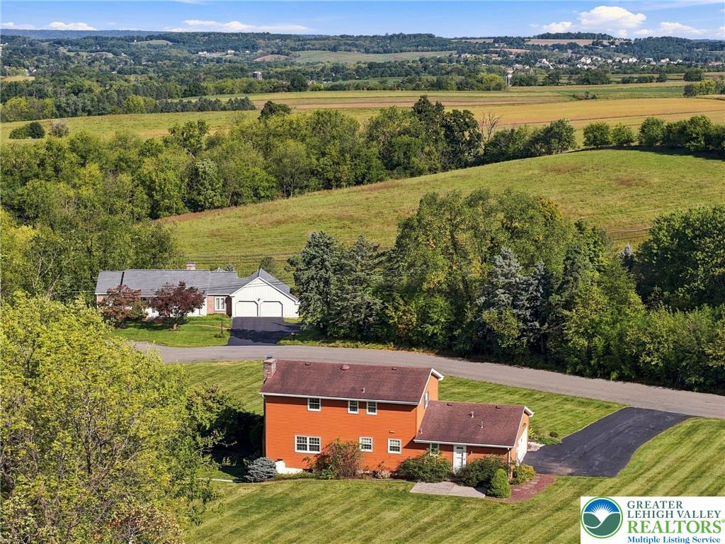 Orange two-story home amid green lawns, wooded hills, and open farmland.