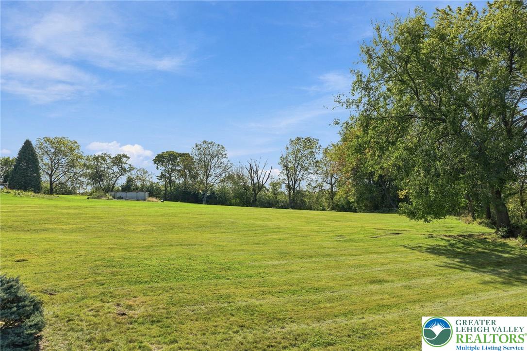 Open grassy property bordered by mature trees, with a small utility structure in the distance.