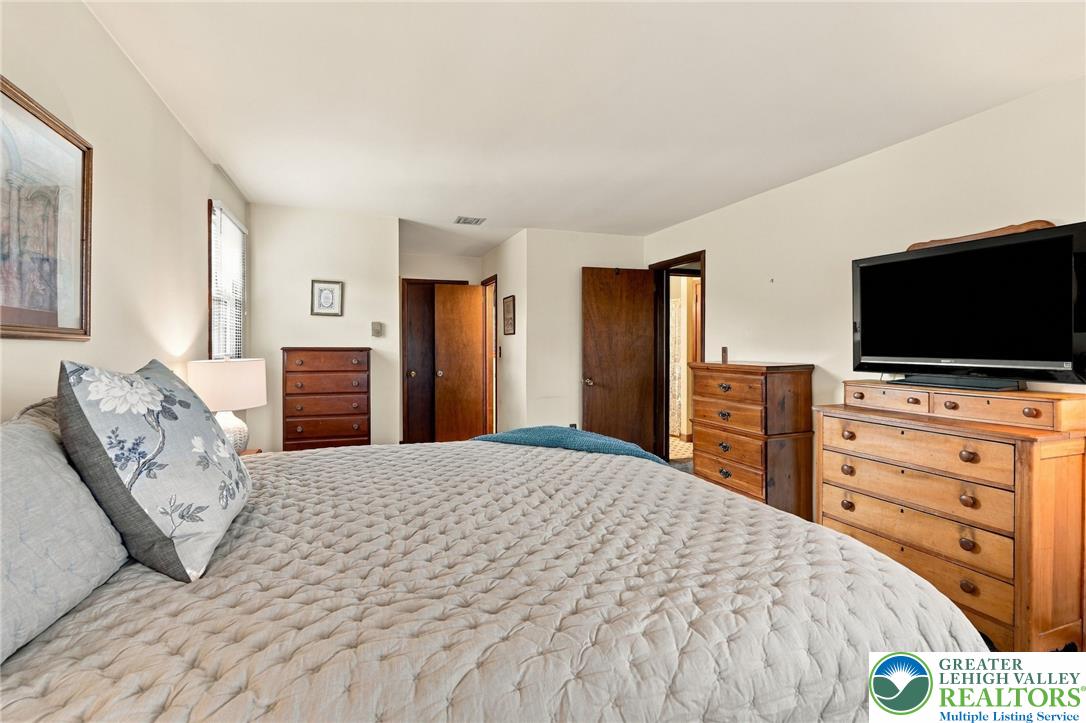 Bedroom with a quilted bed, wooden dressers, and a television.