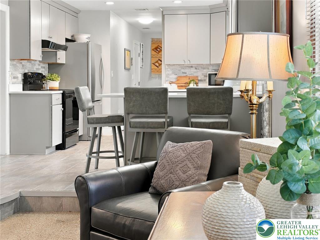 Kitchen and sitting area with a breakfast bar, gray stools, and a dark leather armchair.