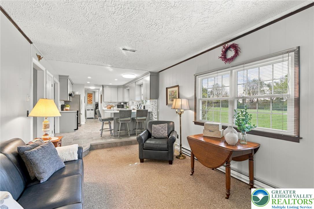 Living room with a leather sofa and armchair, opening to a kitchen with a breakfast island.