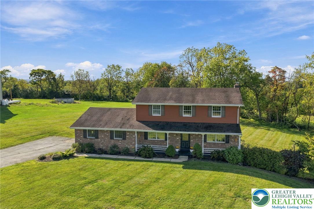 Two-story brick and red-sided home with a broad lawn and trees behind it.