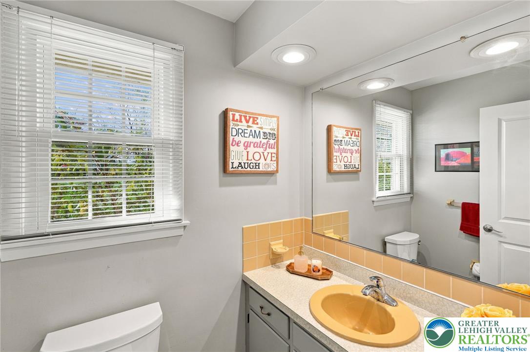 Bathroom with a yellow sink and tile backsplash, wide mirror, and window with white blinds.