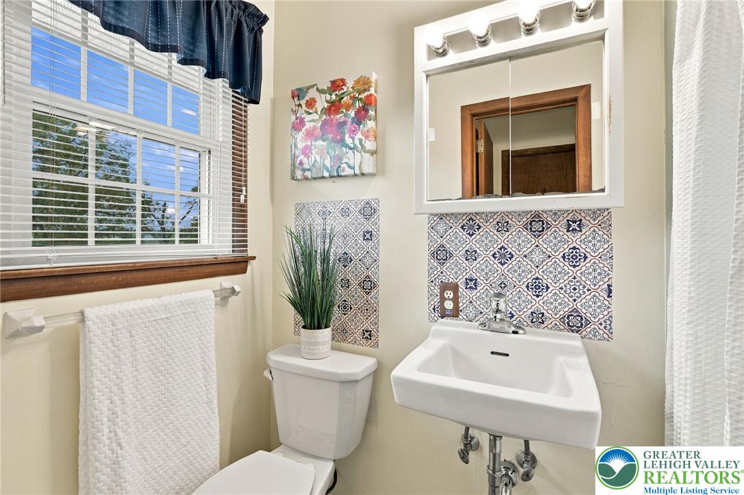 Bathroom with a wall-mounted sink, patterned tile backsplash, and large window with blinds.