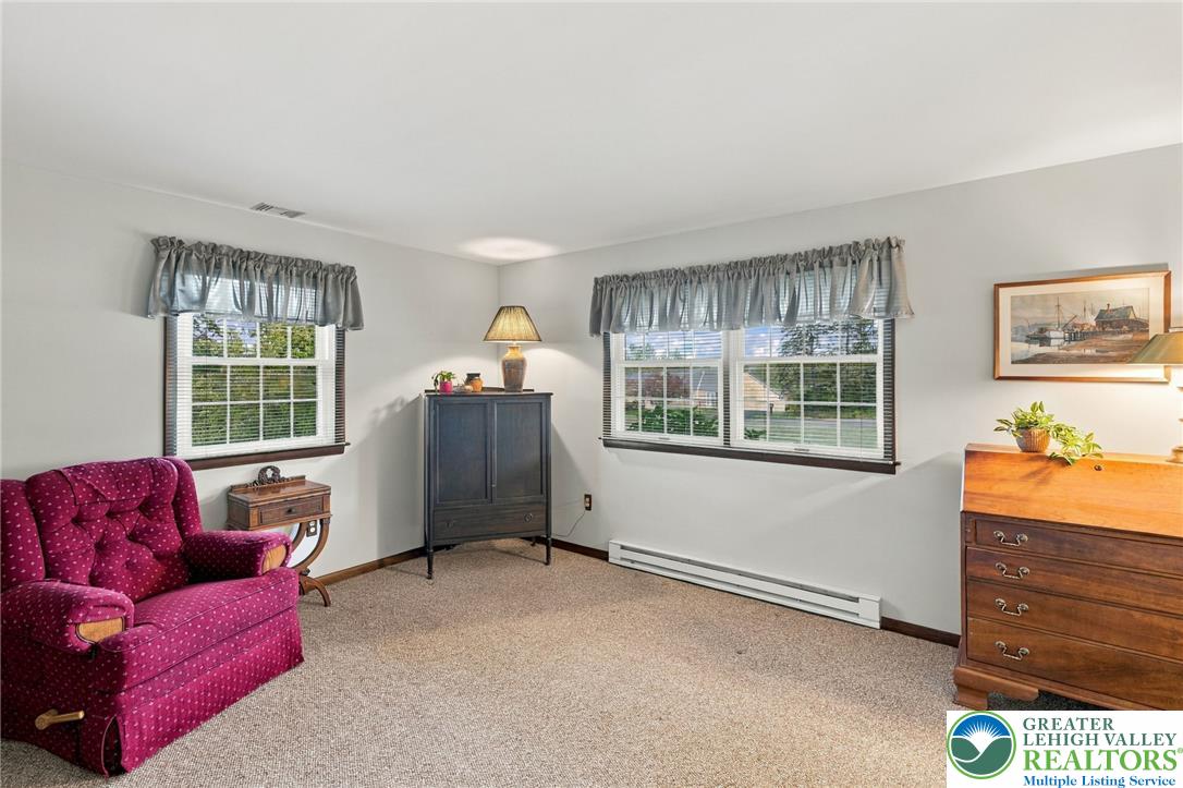 Furnished sitting room with a magenta armchair, dark cabinet, and two curtained windows.