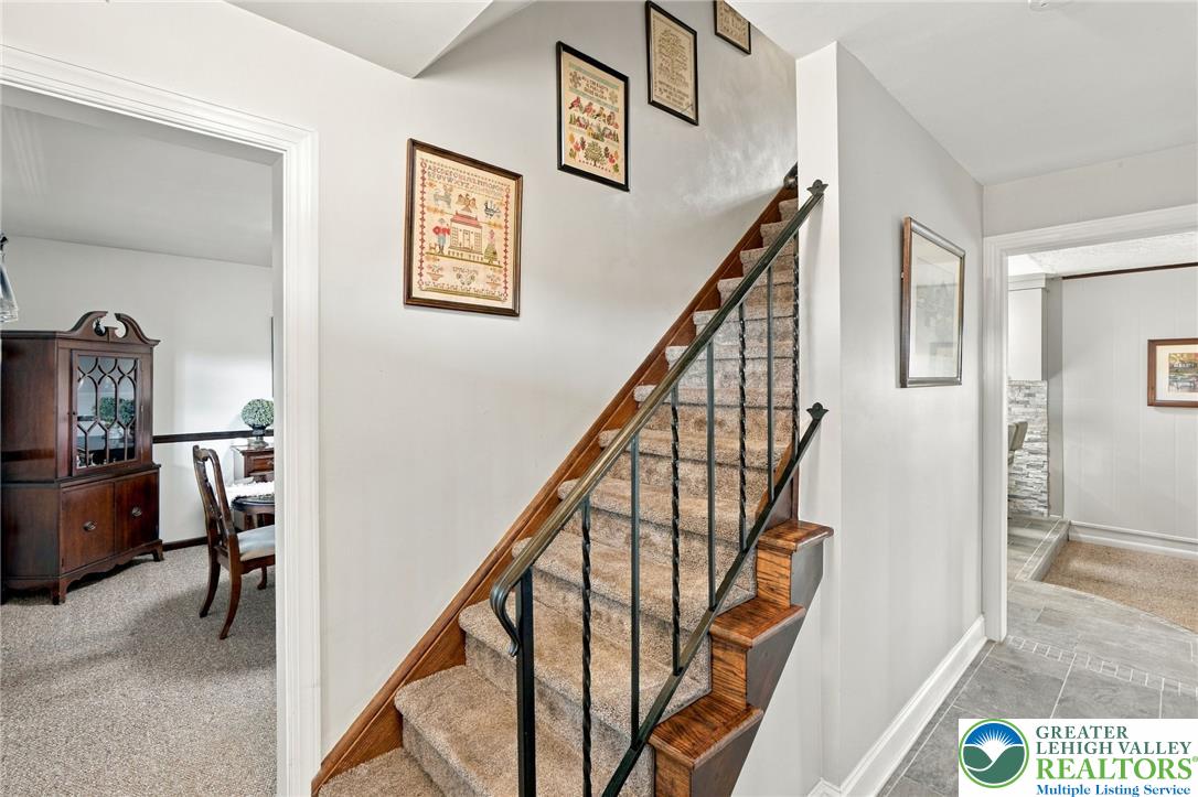 Carpeted staircase with wood handrail and black metal balusters, framed artwork, and adjoining rooms.