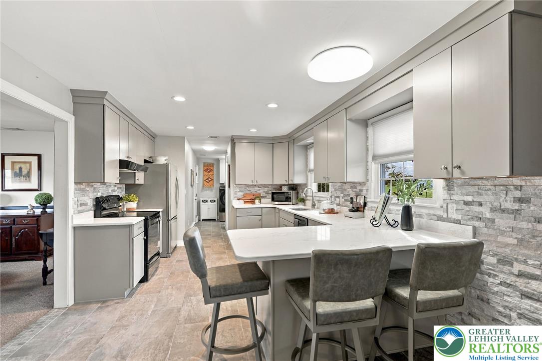 Updated kitchen with gray cabinets, stone backsplash, and a large white island with bar seating.
