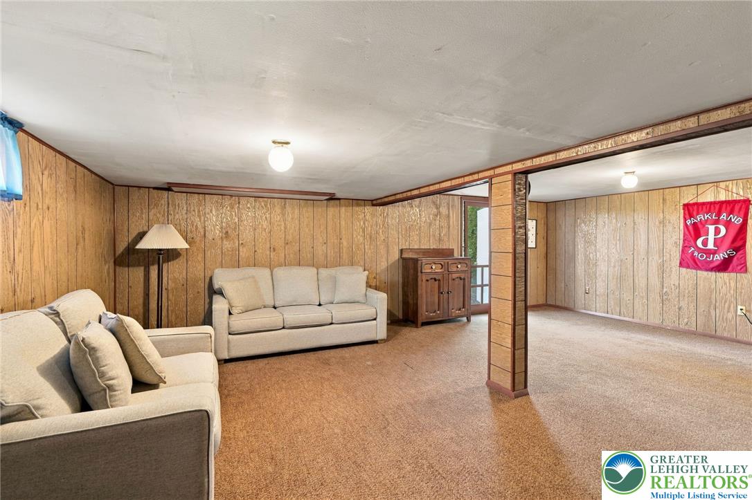 Living area with wood-paneled walls, beige carpet, two sofas, and a Parkland Trojans banner.