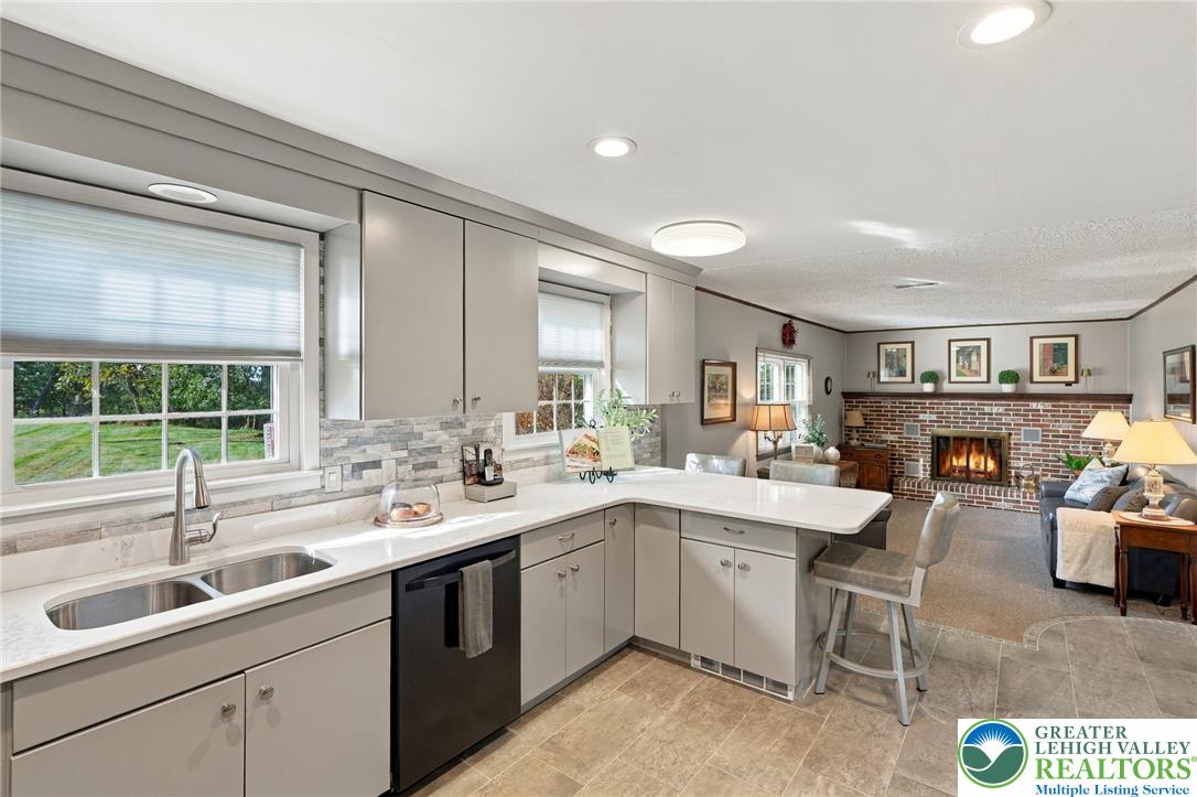 Kitchen with white cabinetry and breakfast bar opening to a living room with a brick fireplace.