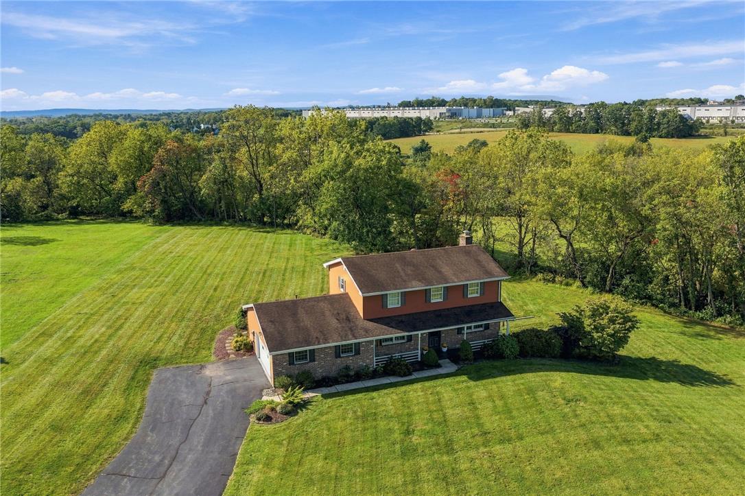 Aerial view of a two-story home surrounded by a broad lawn and wooded backdrop.