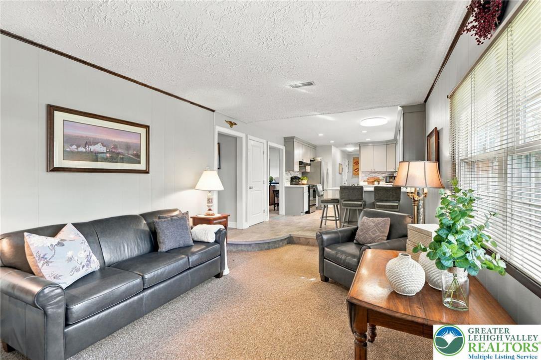 Furnished living room with black leather seating, large windows, and an open kitchen beyond.