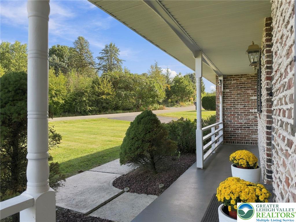 Covered brick-house porch with white columns, yellow chrysanthemums, and a view of the lawn and trees.