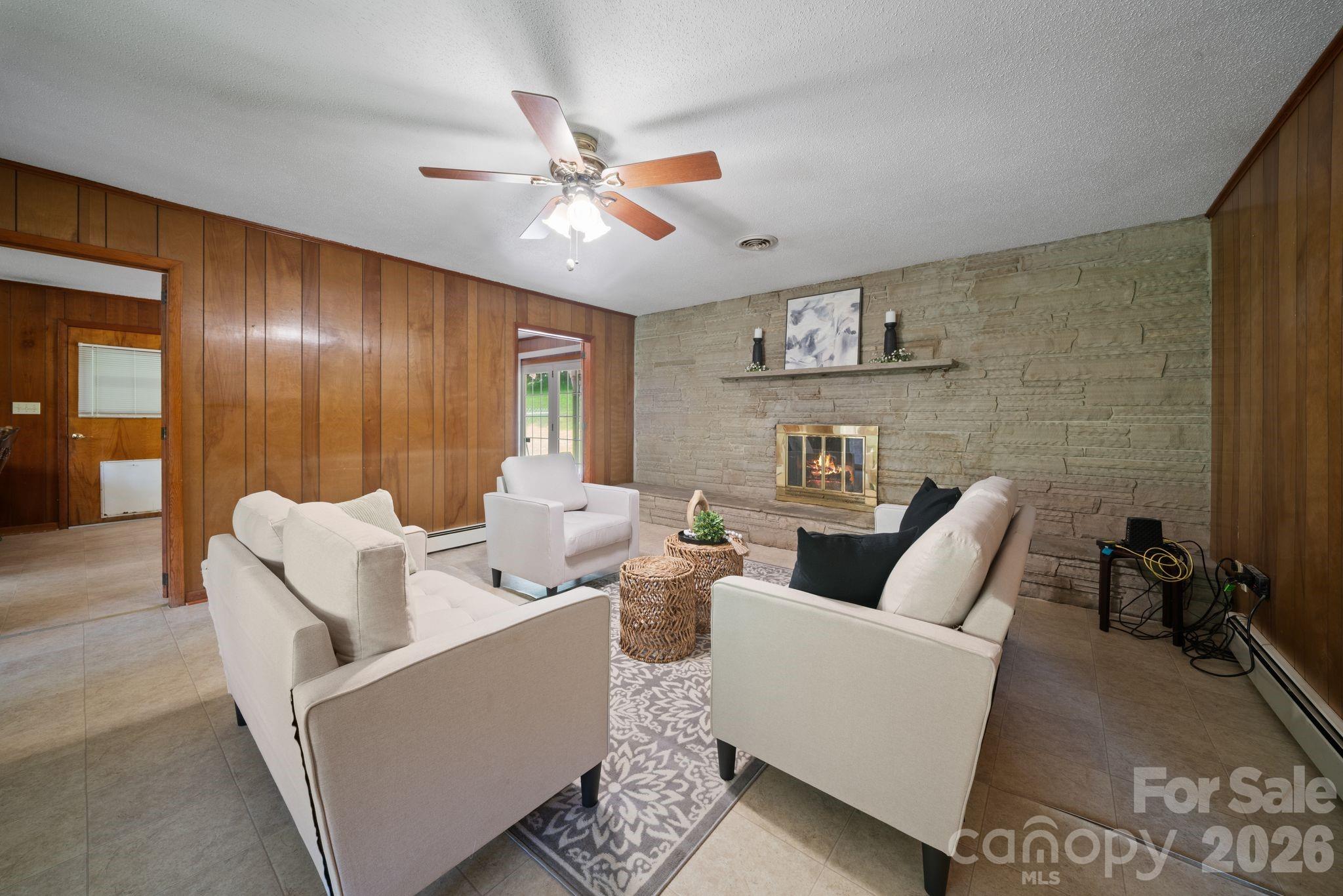 Staged living room with a stone fireplace, wood-paneled walls, and cream seating.