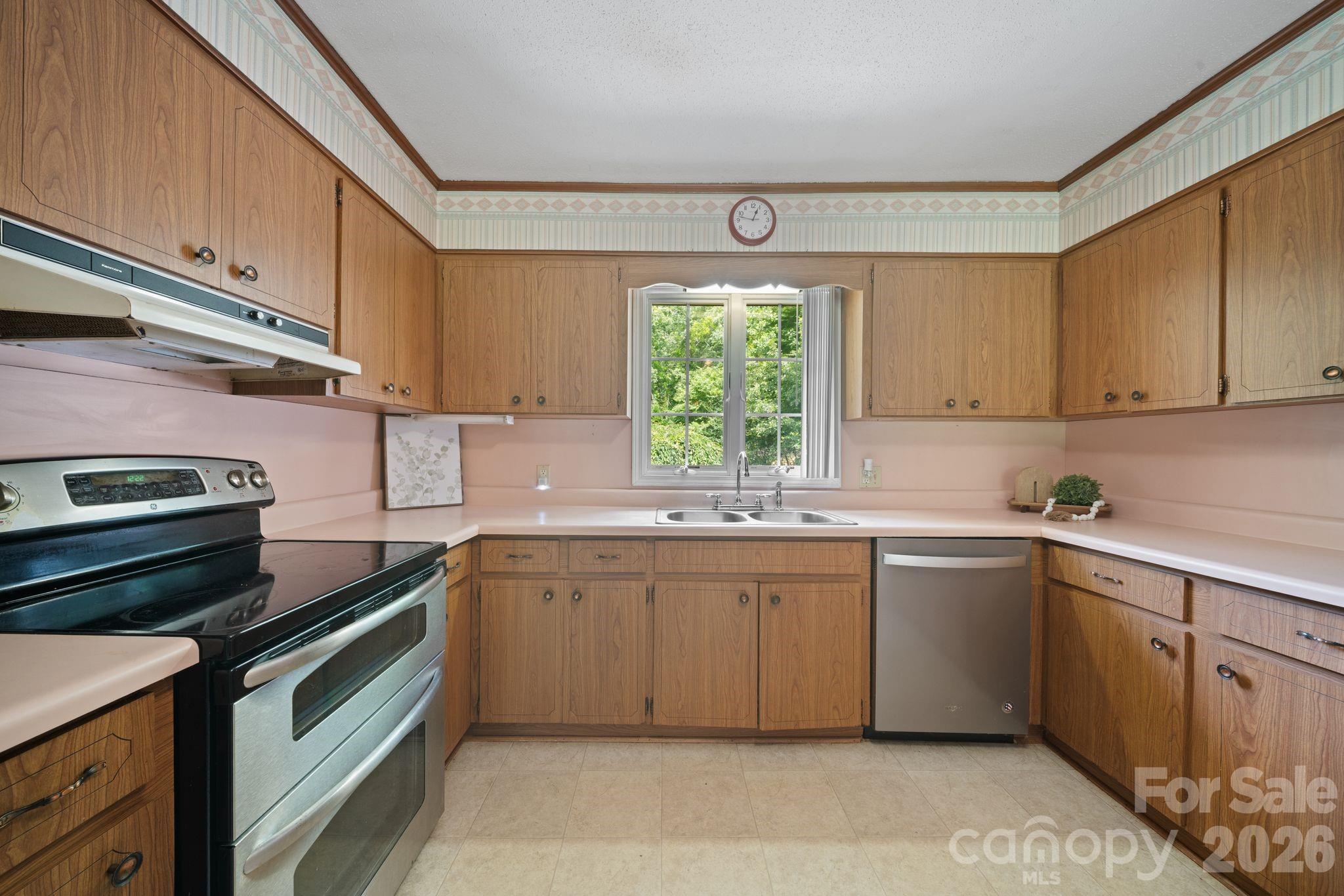 Kitchen with wood cabinets, pink countertops, and a window above the double-basin sink.