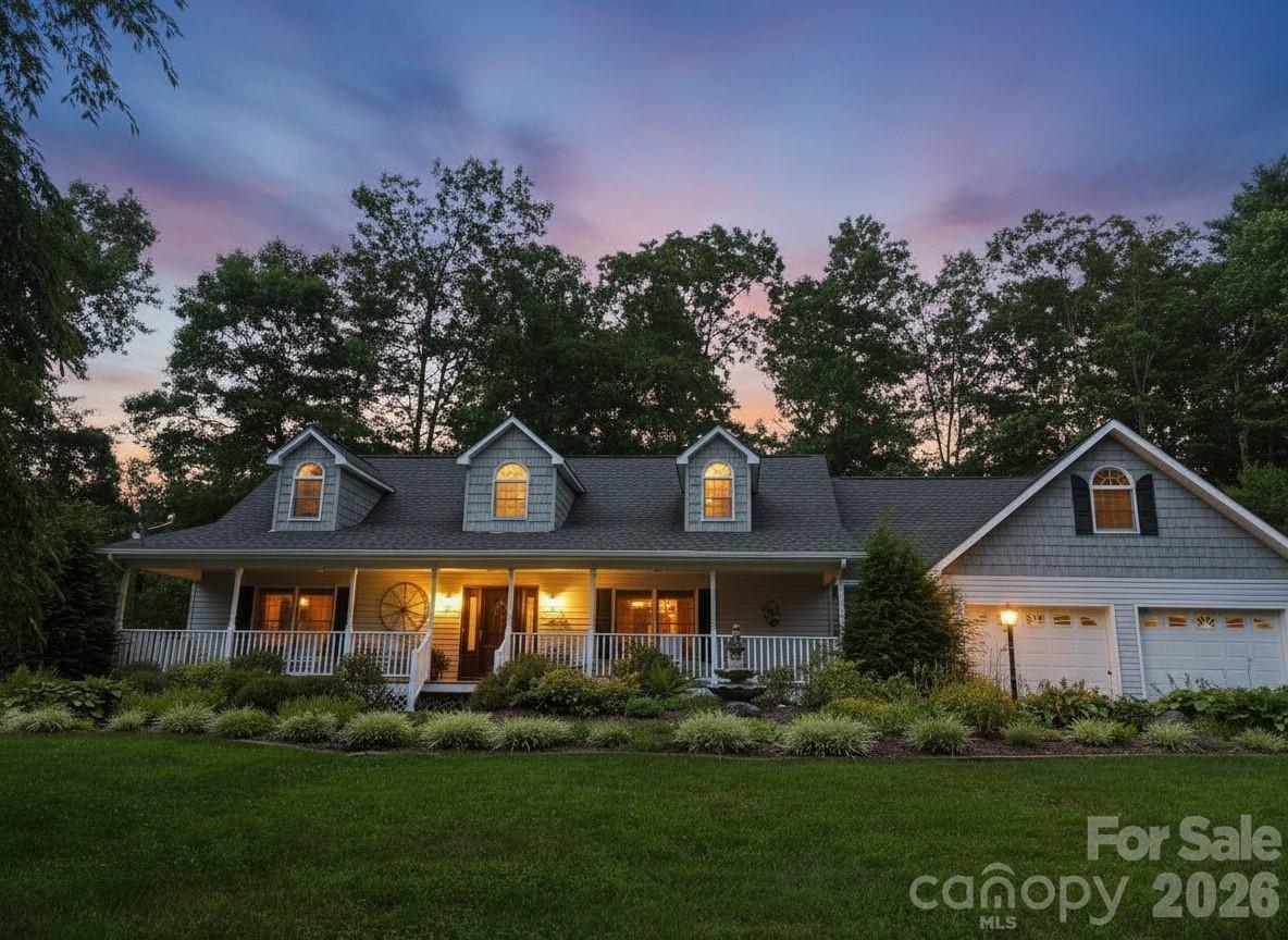 Gray home with glowing dormer windows, a covered porch, and an attached garage at dusk.