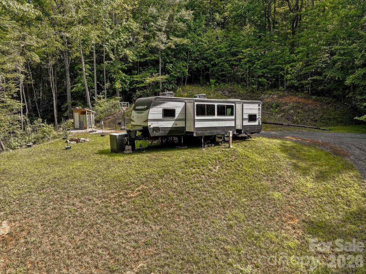 Travel trailer on a grassy wooded lot beside a small shed and basketball hoop.