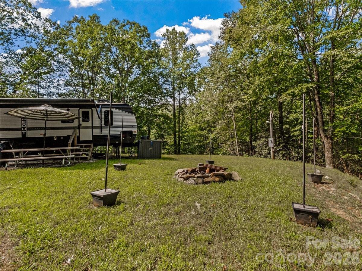 Travel trailer in a wooded grassy clearing with a picnic table and stone fire pit.