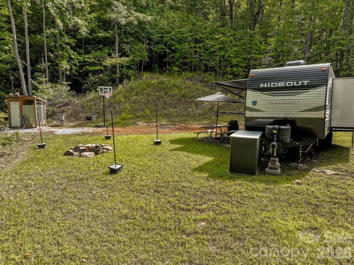 Wooded campsite with a Hideout travel trailer, basketball hoop, fire pit, and picnic table.