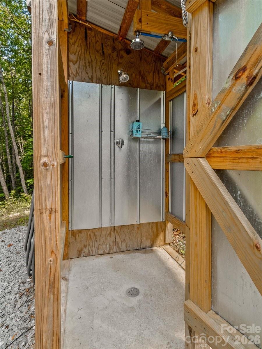 Outdoor shower with two showerheads in a wood-framed enclosure beside the trees.