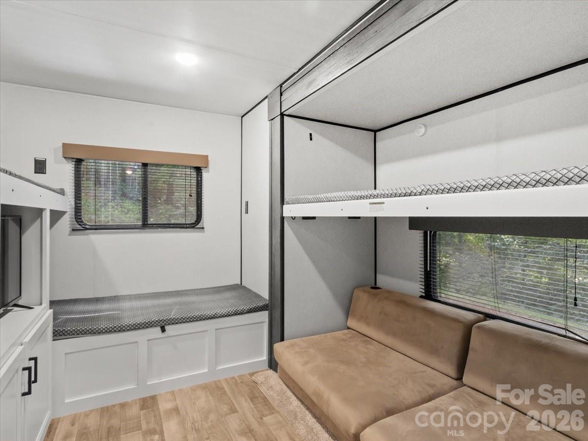 Sleeping area with a raised bunk, built-in bed, and tan sofa beside wide windows.
