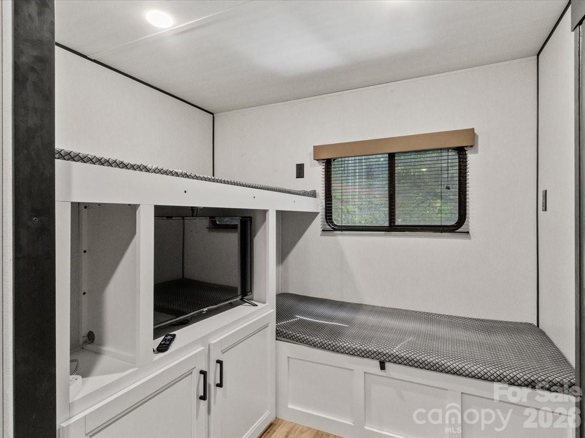 Bedroom with a built-in bed, storage cabinetry, recessed television, and window with blinds.