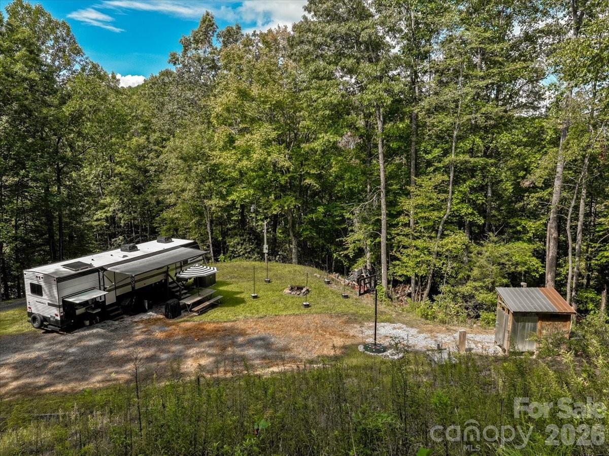 Wooded property clearing with a travel trailer, gravel drive, and small shed.