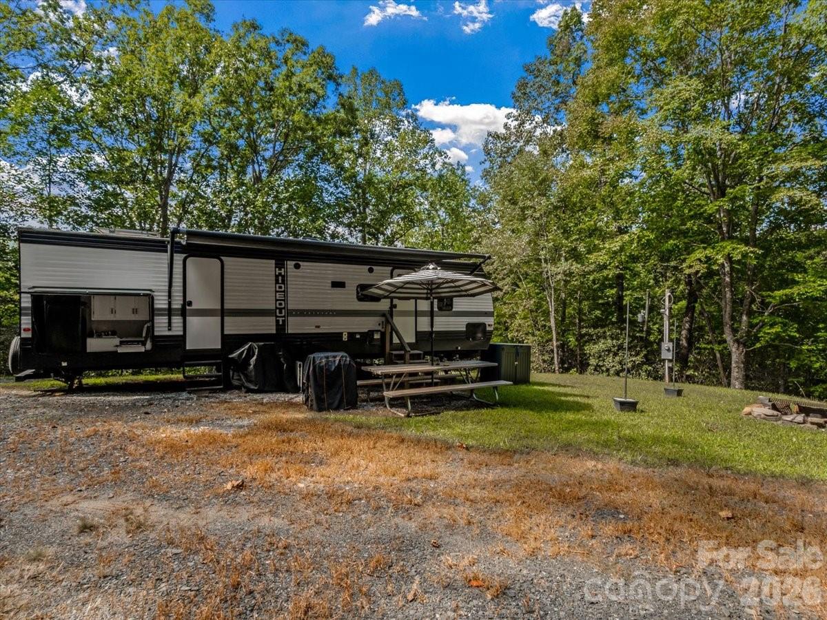 Travel trailer in a wooded clearing, with an awning and picnic table beside it.