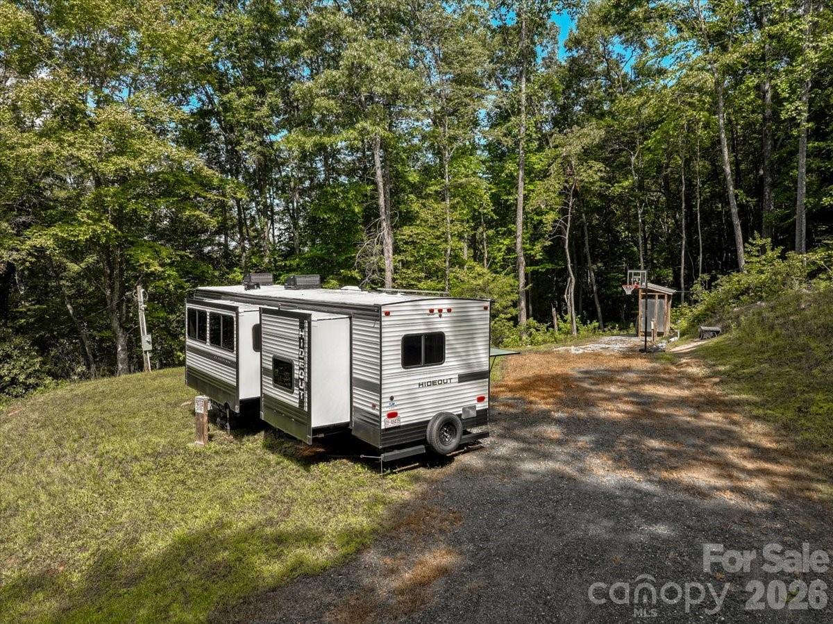 Hideout camper trailer on a wooded lot beside a gravel drive and basketball hoop.