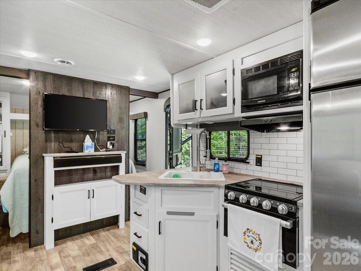 Compact RV kitchen with white cabinets, stainless appliances, and a television beside the sleeping area.