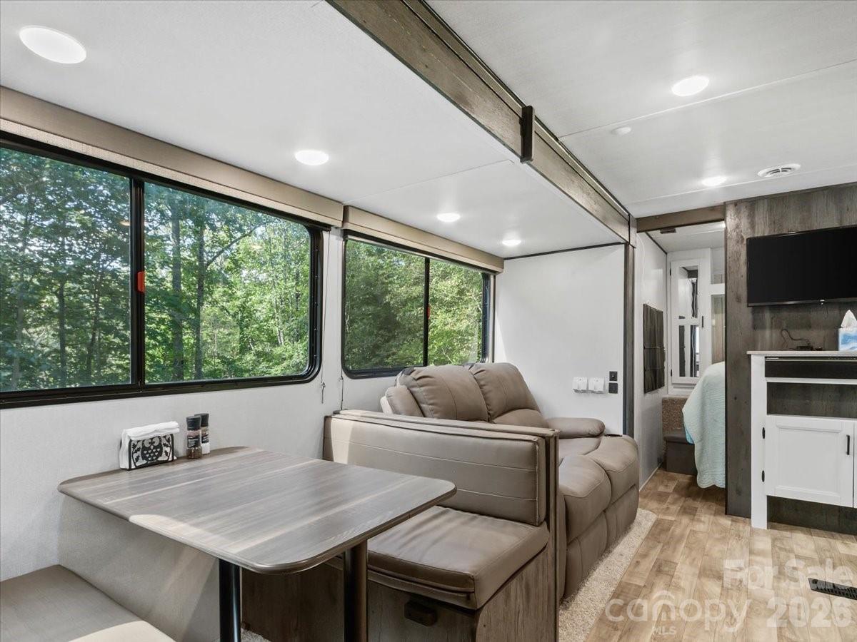 Furnished living and dining area with a gray dinette, tan sofa, and large windows overlooking trees.