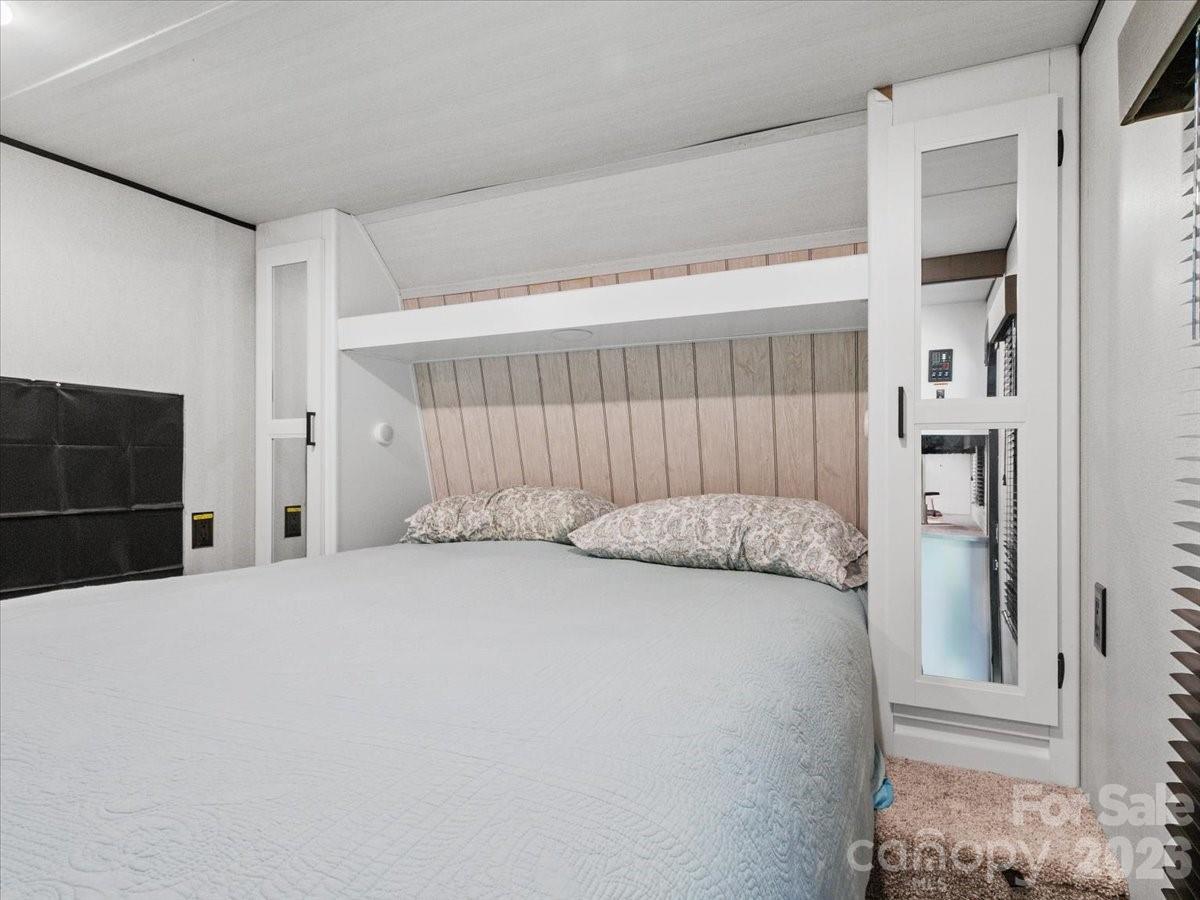 Bedroom with a large bed beneath a built-in loft structure and mirrored panels.
