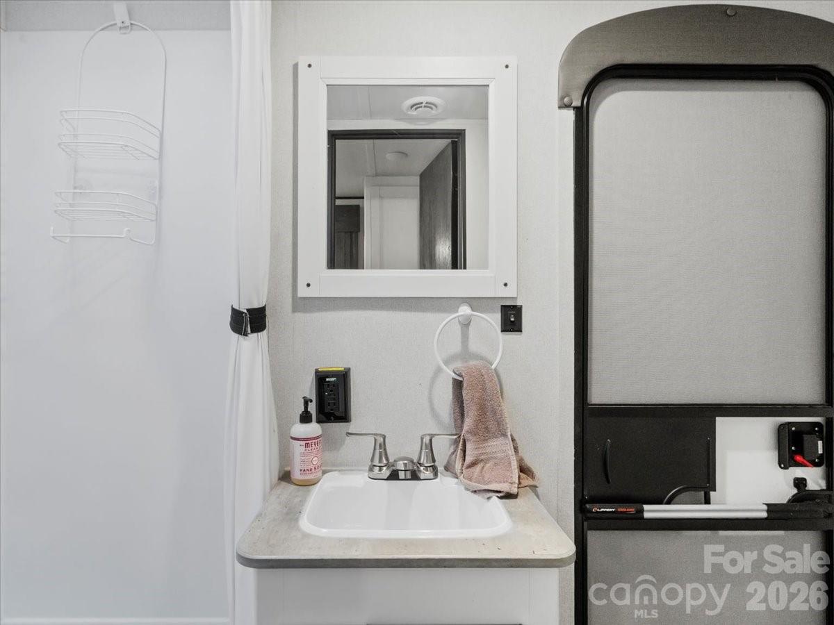 Compact bathroom with a white sink, wall mirror, shower curtain, and towel ring.