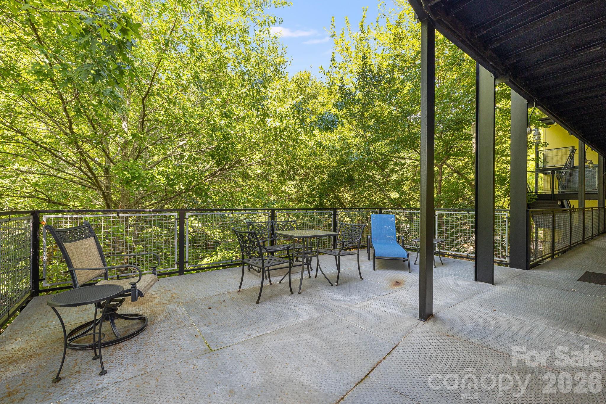 Covered deck with patio furniture and a blue lounge chair overlooking leafy trees.