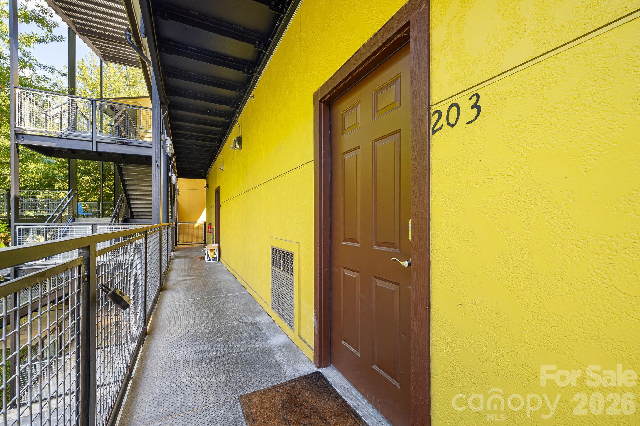 Condominium entry 203 in a yellow exterior corridor with metal railings and stairs.