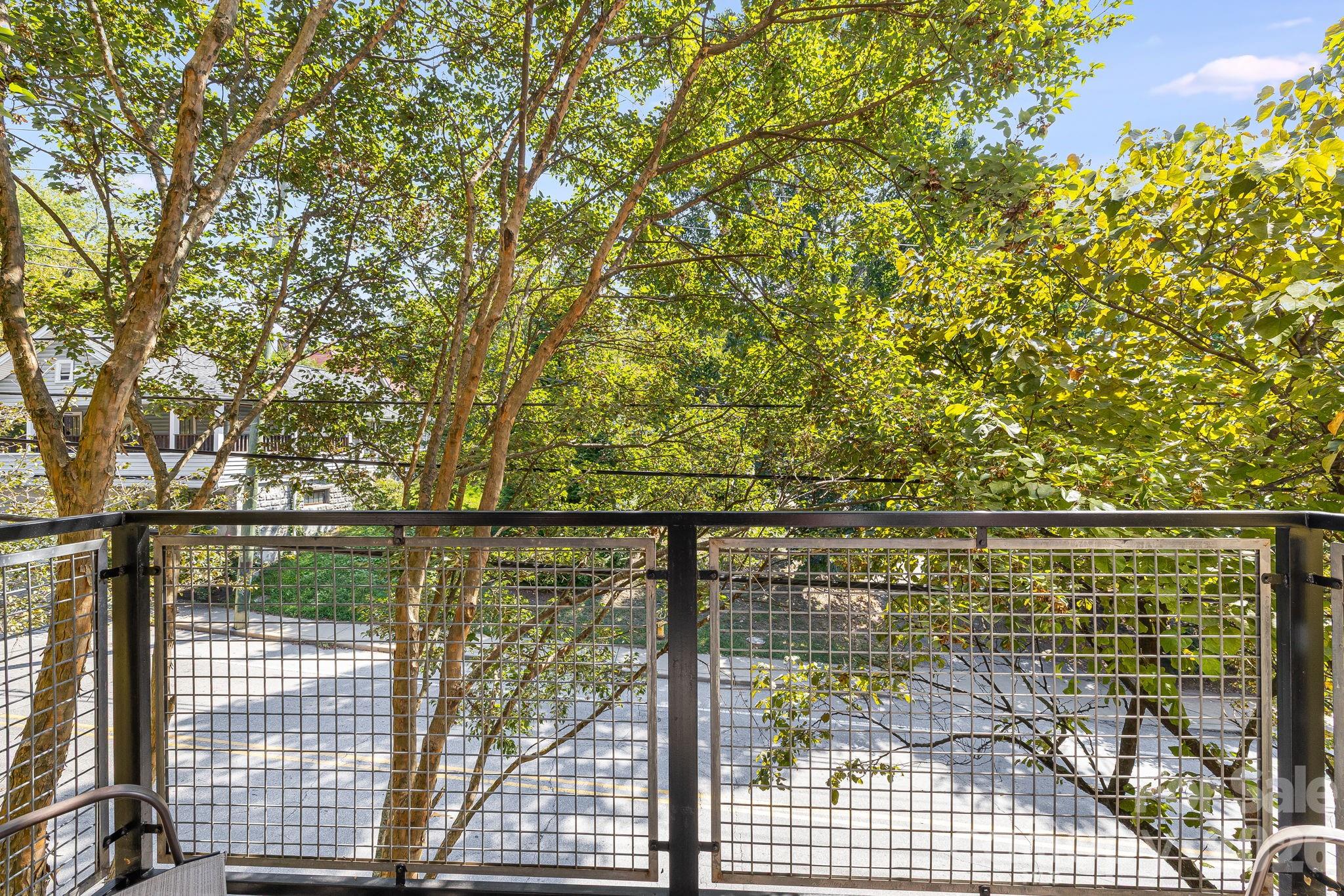 Condo balcony overlooking leafy trees and a quiet street, with a black metal railing.