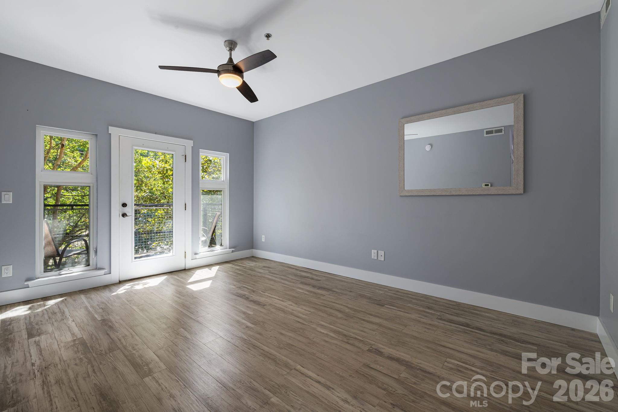 Vacant room with wood-look floors, gray walls, and a glass balcony door framed by windows.