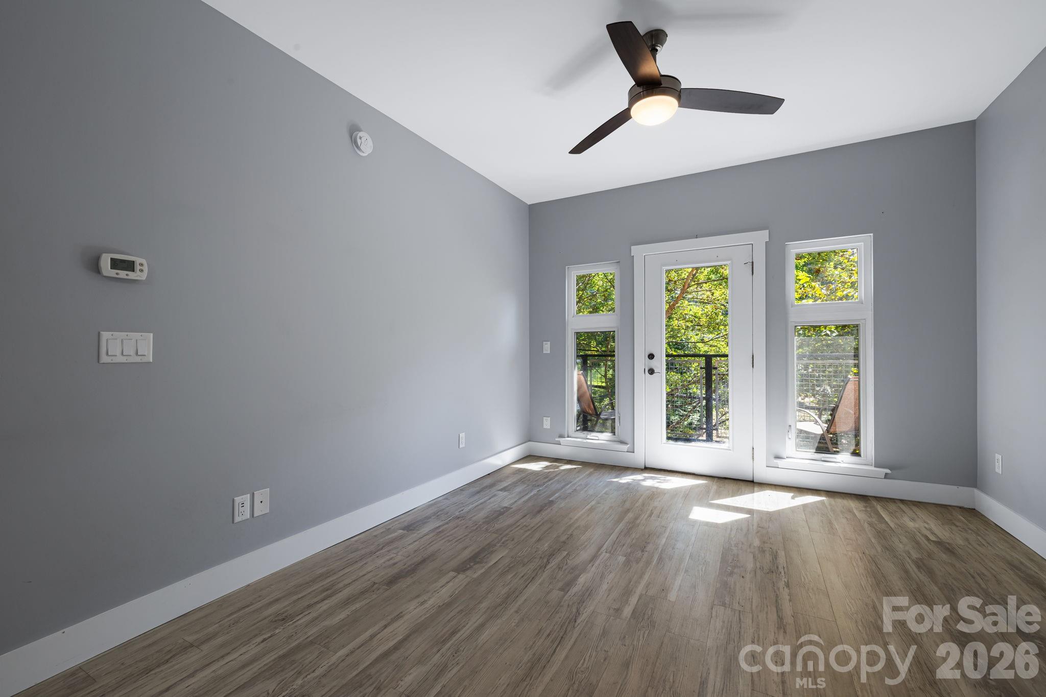 Unfurnished room with gray walls, wood-look flooring, and a glass door opening onto a tree-lined balcony.