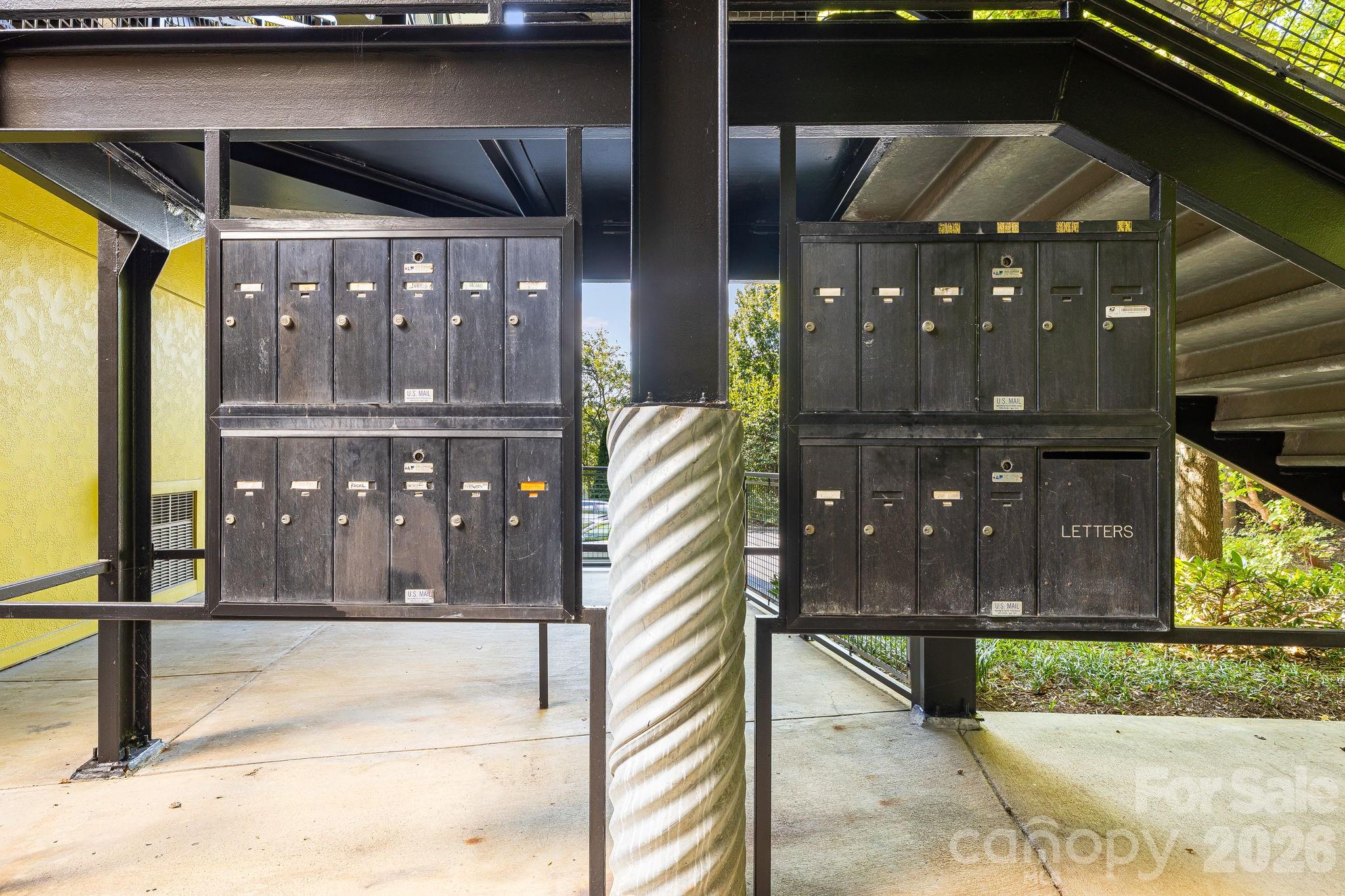 Condominium mailboxes beneath a covered walkway, beside a spiral-textured column and exterior stairs.