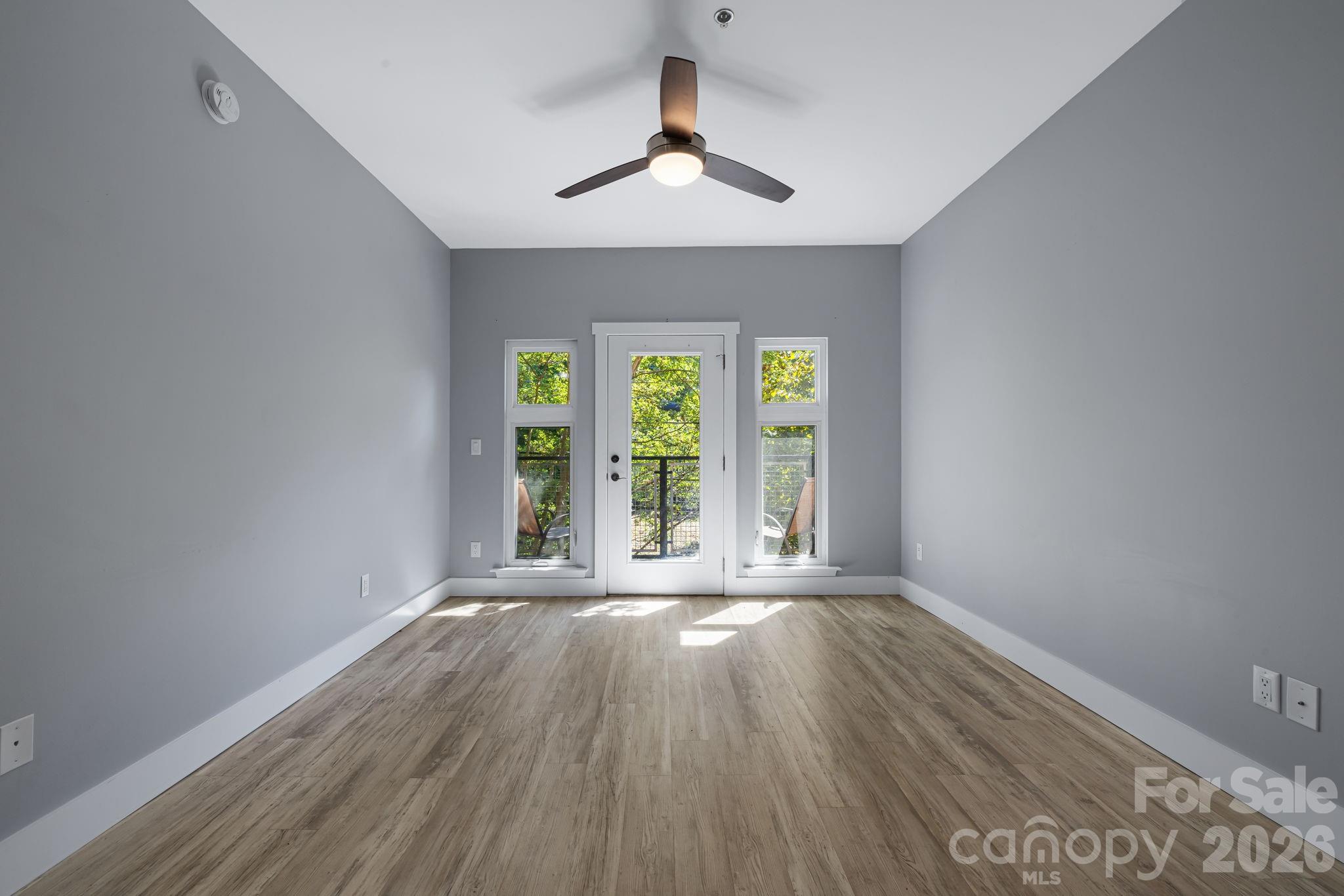 Empty room with wood-look flooring and a glass balcony door framed by narrow windows.