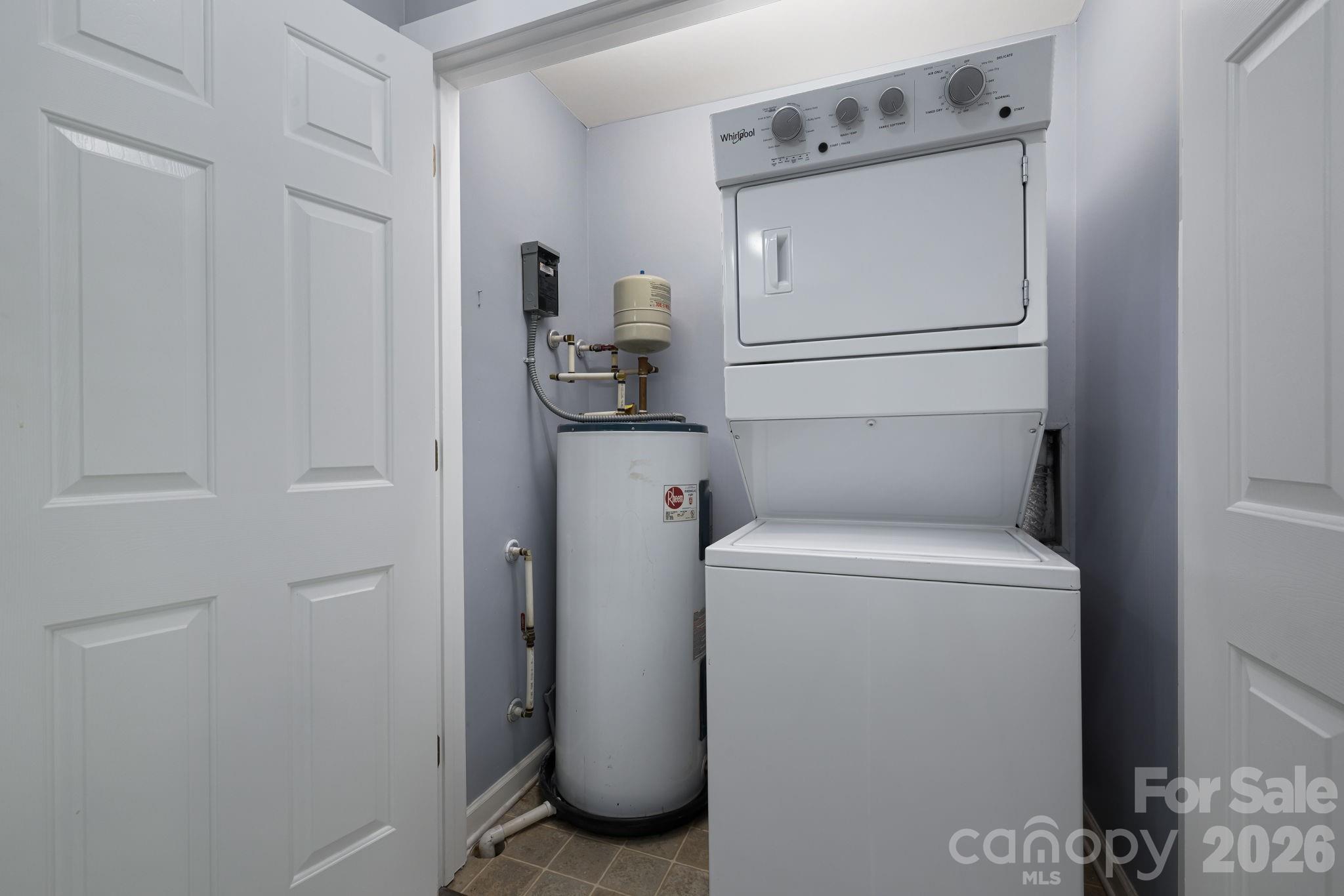Laundry closet with a stacked washer and dryer beside a cylindrical water heater.